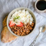 A delicious breakfast bowl with cottage cheese, granola, and strawberries served with black coffee.