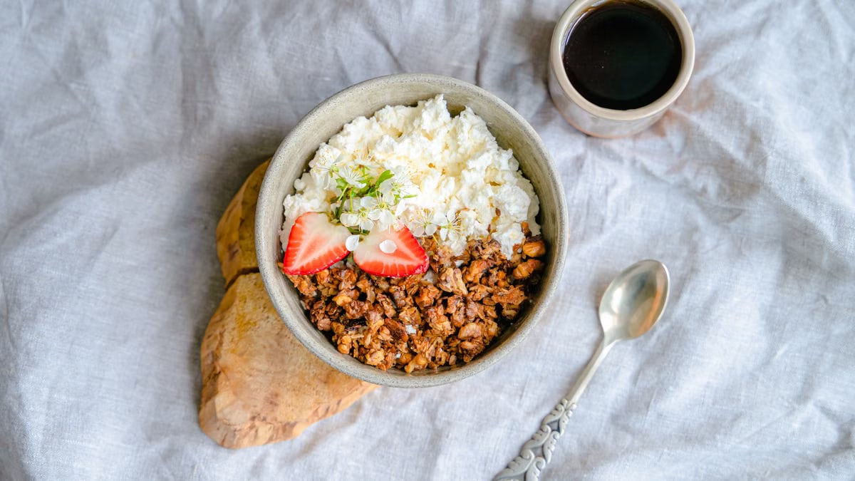 A delicious breakfast bowl with cottage cheese, granola, and strawberries served with black coffee.