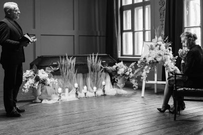 A somber funeral scene in grayscale showing a pastor and woman mourning.