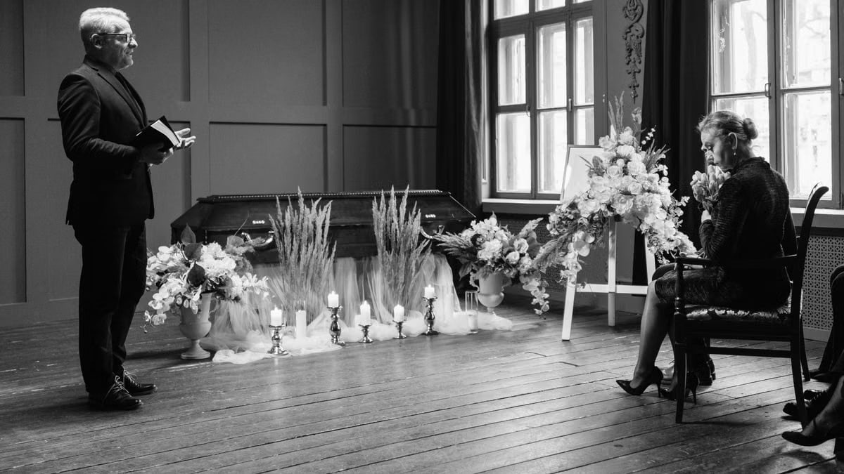 A somber funeral scene in grayscale showing a pastor and woman mourning.